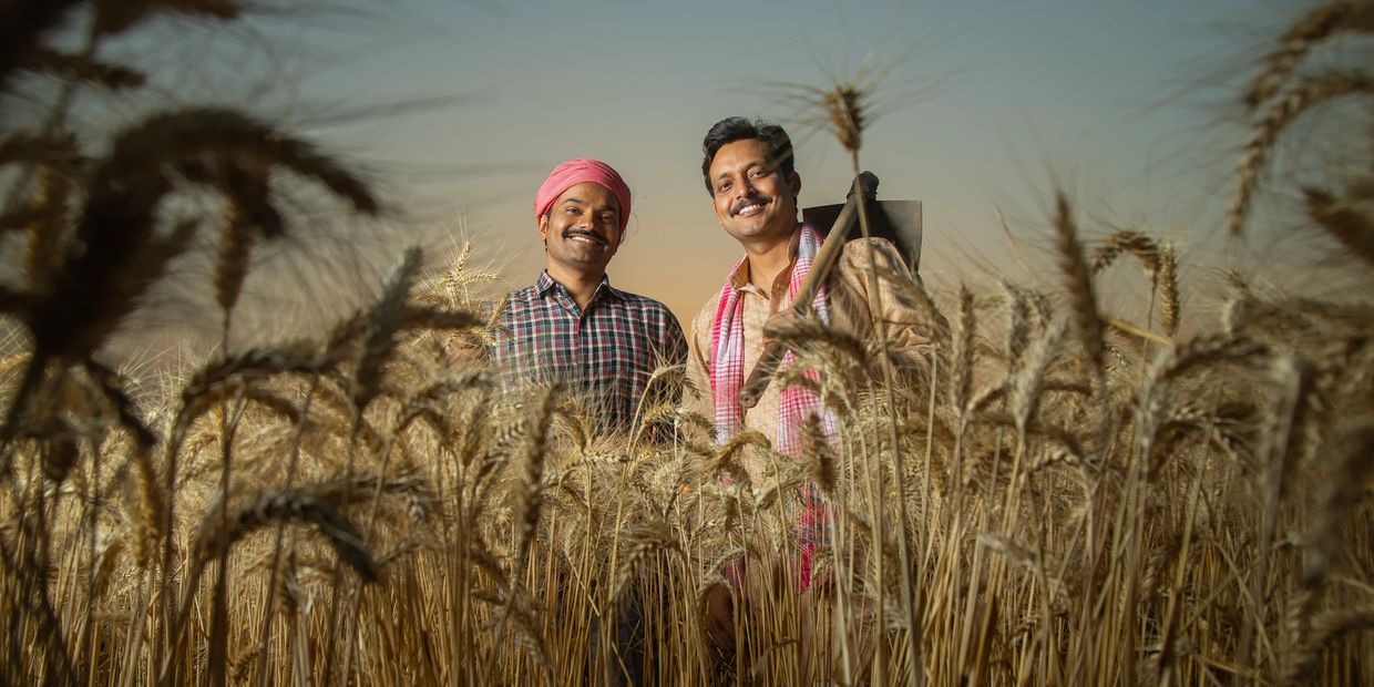 Two smiling farmers standing in a golden wheat field during sunset.