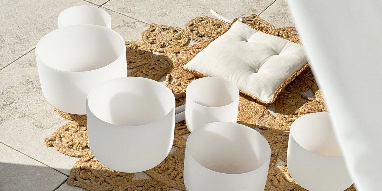 White crystal singing bowls on a woven mat with a cushion.