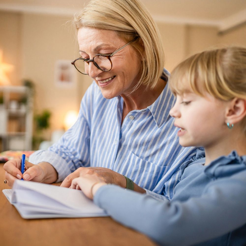 Older woman helping young girl with homework at a table.