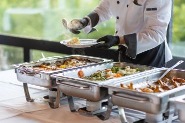 Chef serving food from buffet trays.