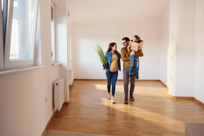 Happy expecting family talking while carrying their belongings in an empty apartment. Copy space.