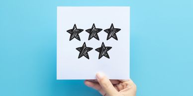 Hand holding a white card with five black sketched stars on a blue background.