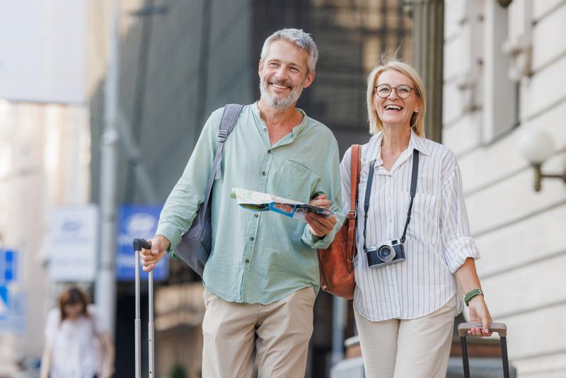 Cheerful mature couple walking through a city street with a map and luggage, enjoying their travel experiences and urban exploration together.