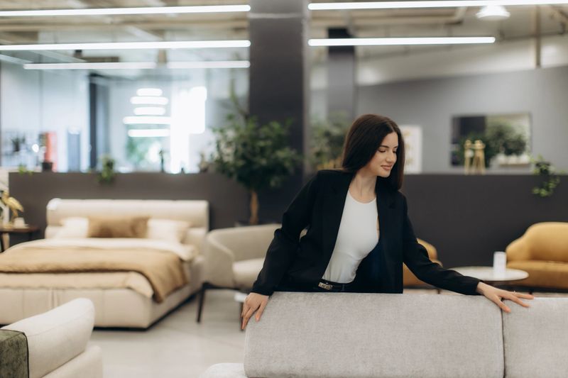 A woman in a furniture store examines a sofa surrounded by a contemporary interior design.