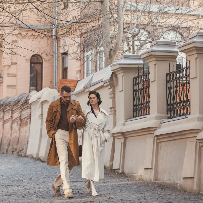 Man and woman dressed in elegant vintage look enjoying each other's company while walking down old street. Concept of joy in motion, retro couple, style, love in everyday moments.
