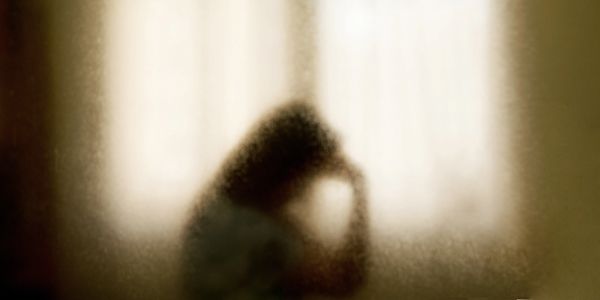Silhouette of a person in distress behind a frosted glass window.