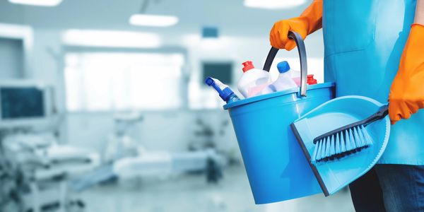 Person holding cleaning supplies in a medical setting wearing orange gloves.