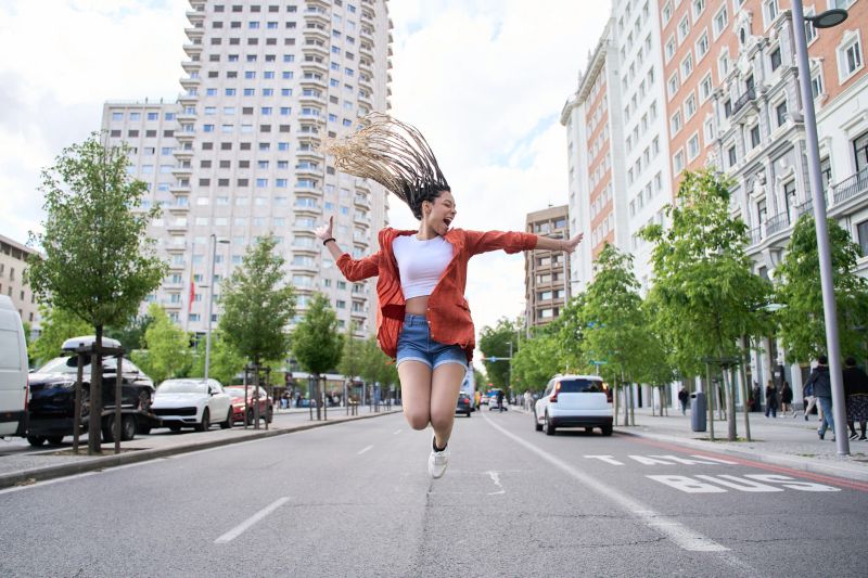 Carefree young latin woman with long braids joyfully jumping in the middle of a city street, expressing freedom and happiness
