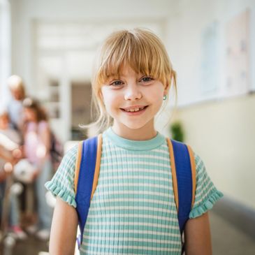 Smiling young girl with backpack in school hallway.