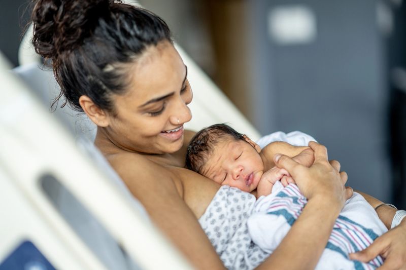 A mother lovingly cradling her newborn baby while resting in a hospital room, conveying maternal love and bonding immediately after childbirth, with a focus on family connection and nurturing care.