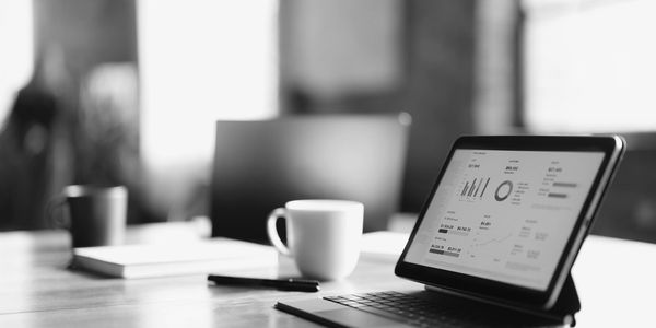 Tablet displaying graphs and data on a desk with a coffee cup.