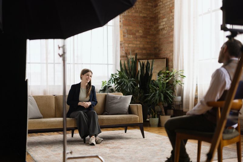 Young businesswoman sitting comfortably on a modern sofa, engaging in an insightful interview with a journalist in a stylish loft setting