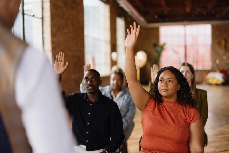 Diverse group of students raising hands enthusiastically, seeking answers during an engaging lecture in a university classroom setting