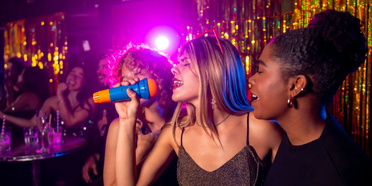 Friends singing karaoke together in a vibrant party setting.