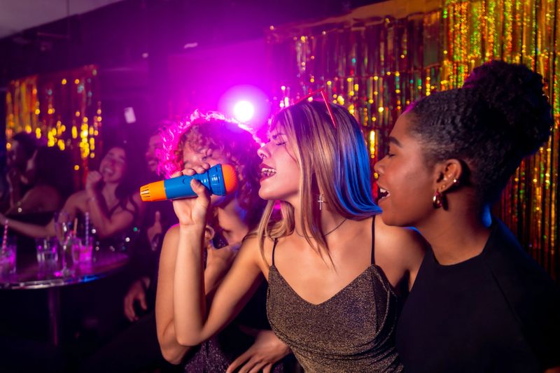 Multi-ethnic group of female friends laughing and singing together during a lively karaoke night at a vibrant nightclub, enjoying the festive atmosphere