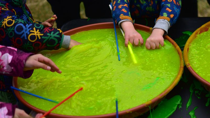 Children hands closeup playing with neon green slime in a large sensory bin during an outdoor activity. Hands-on sensory play promoting tactile exploration, creativity, and fine motor skills. no face