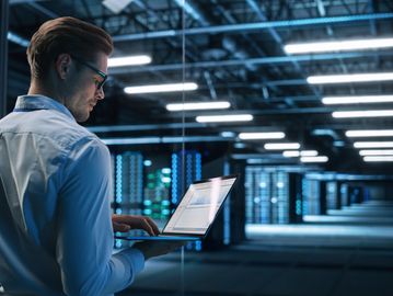 Man working on laptop in a data center with server racks.