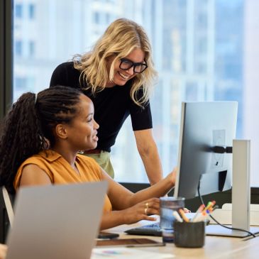 Two women collaborating at a desk with a computer.