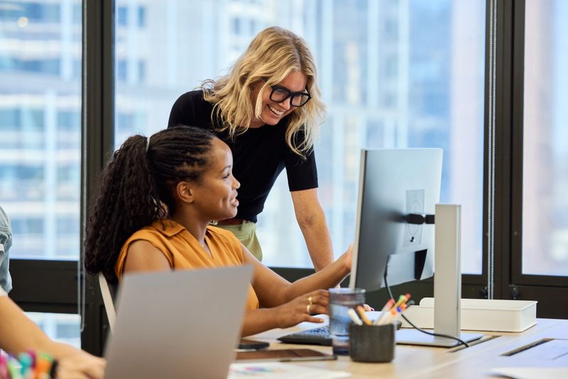 Smiling female employee explaining strategies to manager through computer. Businesswomen are working together in office. They are examining data.