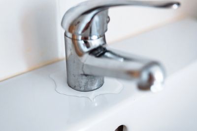 Close-up of a leaking faucet with water on the sink.