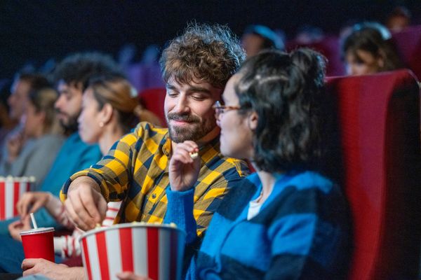 Couple sharing popcorn and enjoying a movie in a theater.
