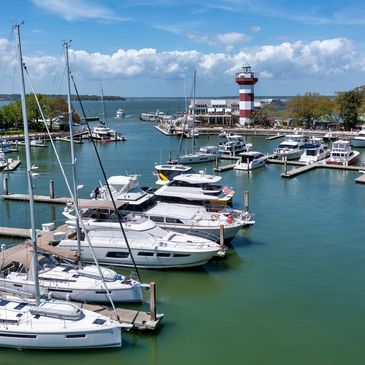 Boats docked in a calm marina with a red and white lighthouse in the background.