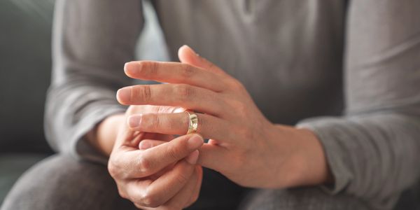 Person removing a gold ring from their finger, wearing gray clothing.