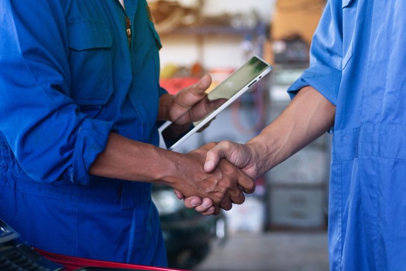 Close up hand of two mechanics shaking hands, collaboration concept, one person has a tablet in his hand.