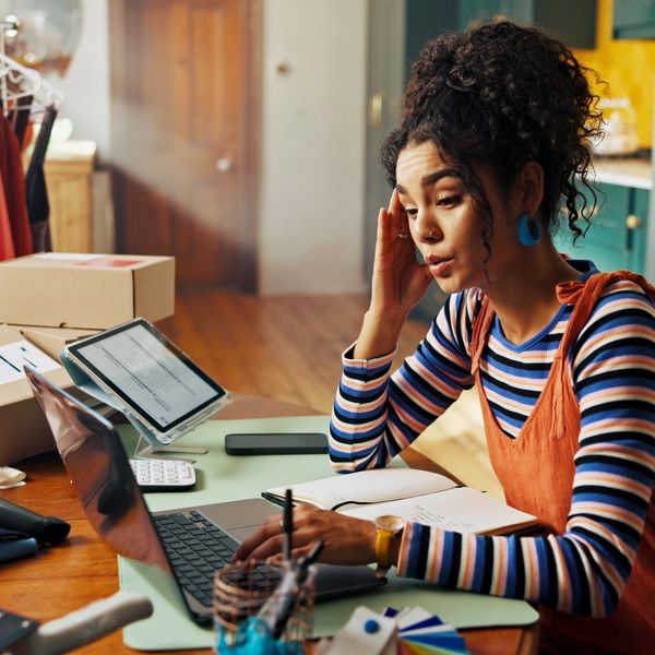 A young woman working on a laptop surrounded by clothes and shipping boxes.