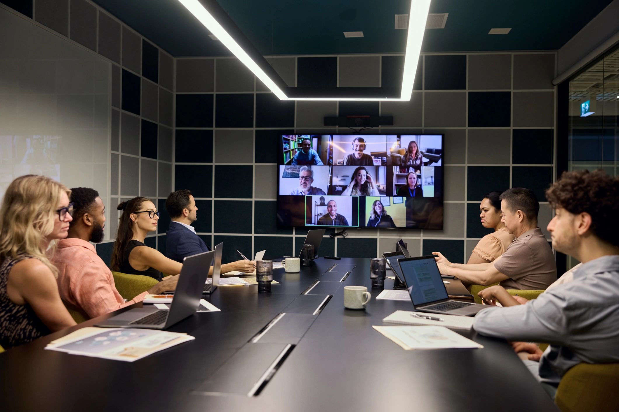 Diverse group in a conference room attending a hybrid meeting with remote participants on a screen.