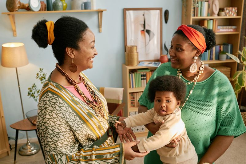 Two African American women enjoying conversation while holding playful baby during family gathering at home