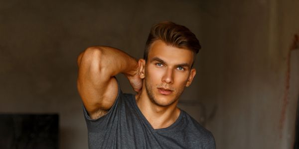 Young man with blue eyes posing with hand behind head.