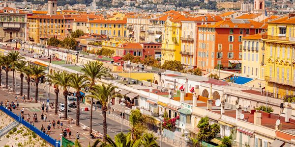 Colorful buildings and palm trees line a lively street in a Mediterranean city.