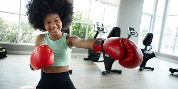 Young girl posing happily with boxing gloves.