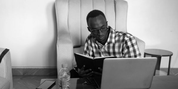 Man reading a book and looking at a laptop.