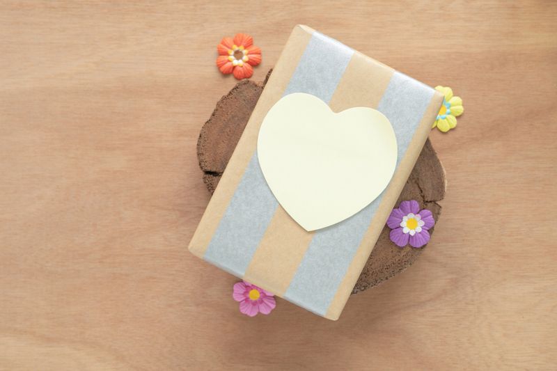 Top view, a gift wrapped in striped paper with a heart-shaped tag for text on a wooden surface and decorated with small flowers. Gift box for concept happy birthday, thank you, Valentine's day.