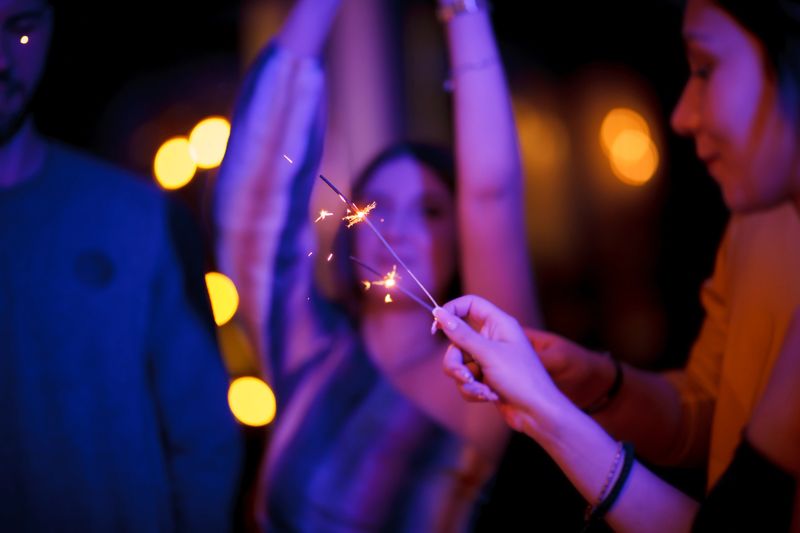 Group of people enjoying a festive night with sparklers, embracing the warm and atmospheric ambiance created by blurred lights in the background.