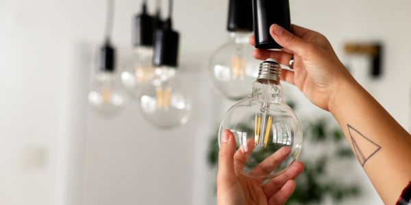 Hands installing a large light bulb with several hanging bulbs in the background.