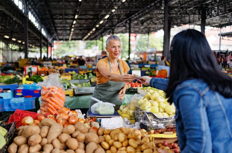 Colorful vegetable selection neatly displayed at a market stall with woman shopping and local vendor selling