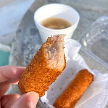 Hand holding a bitten fried snack with a dipping sauce cup in the background.