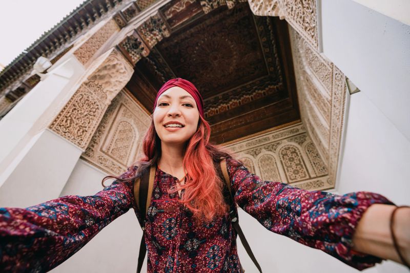 Young woman smiling while taking a selfie in the stunning Bahia Palace, capturing the beauty of Marrakech's culture