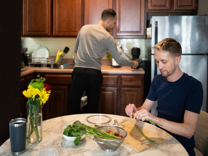 This is a lifestyle photograph of two married gay men in their 30s preparing dinner together at home in their New York City apartment.