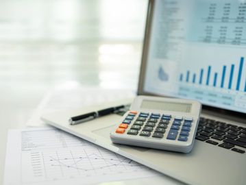 Calculator and pen on laptop with financial charts and graphs.