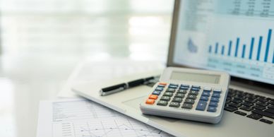 Calculator, pen, and financial charts on a laptop keyboard.