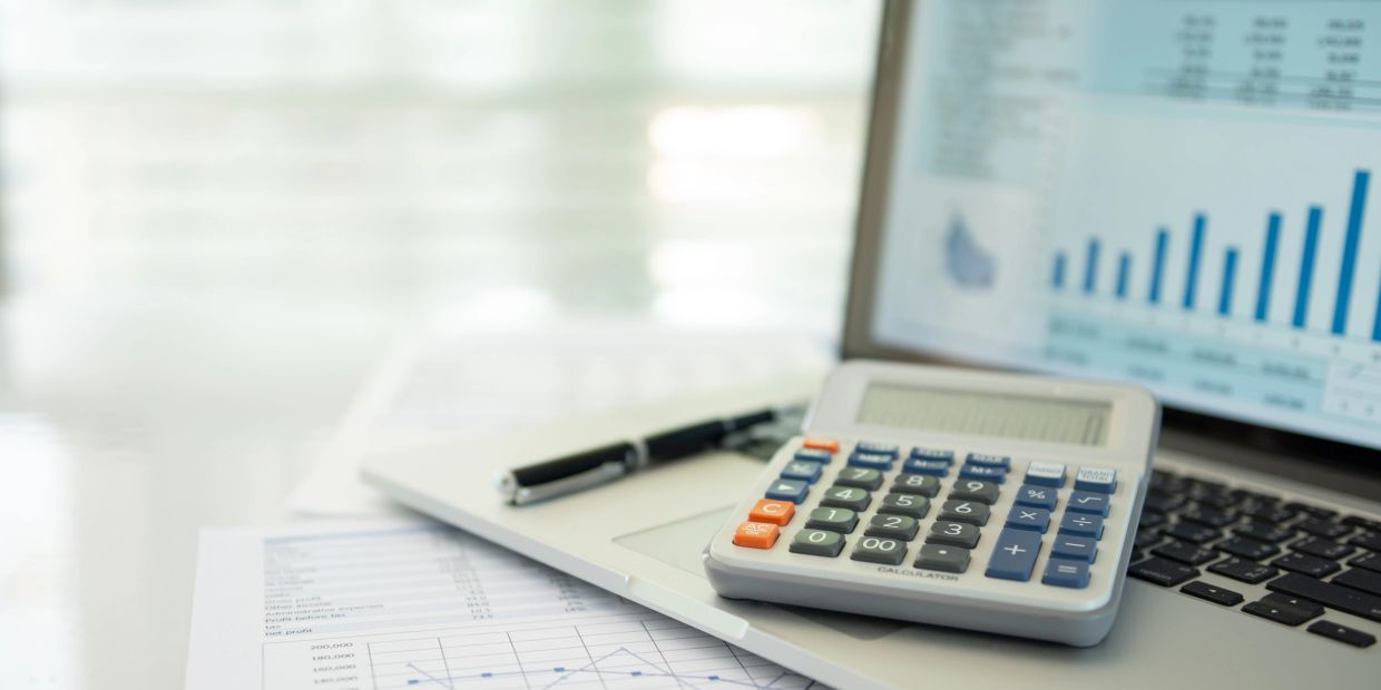 Calculator and pen on laptop with financial graphs and charts.
