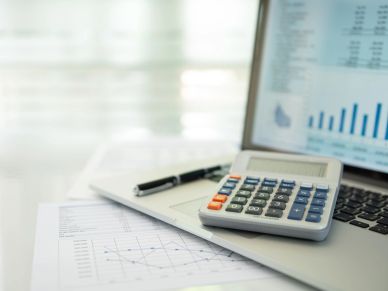Calculator on laptop with financial charts and pen.