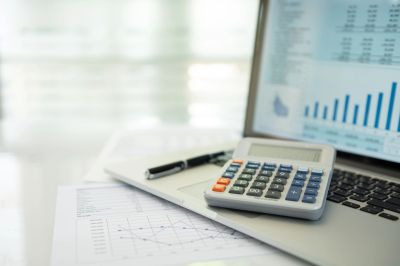 Calculator on laptop with financial charts and pen.