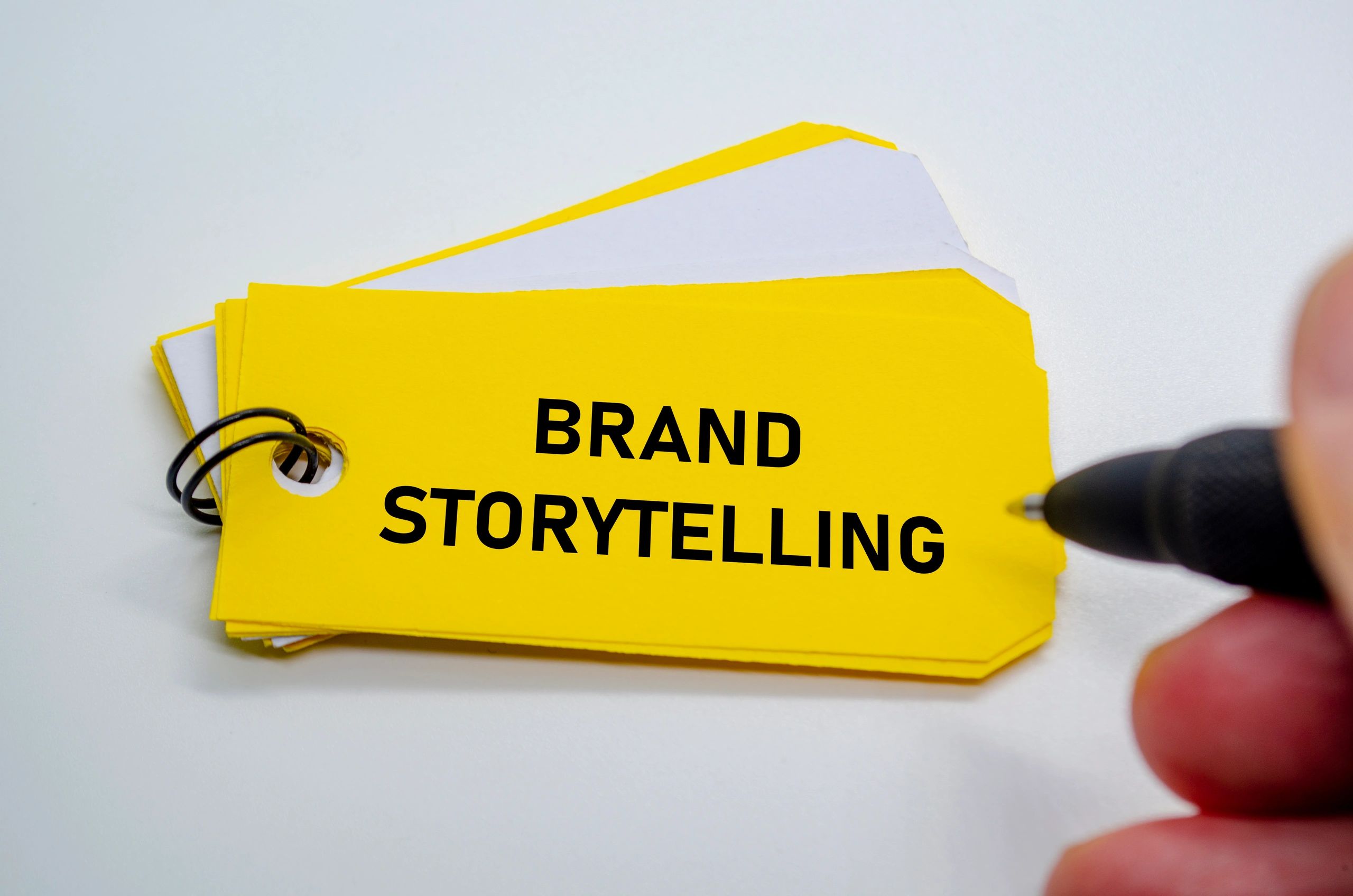 Yellow card with 'Brand Storytelling' text and a hand holding a pen.