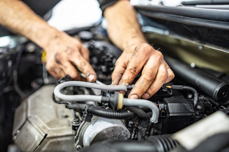 A close-up image of mechanic hands working on a vehicle engine, showcasing maintenance and repairs. The photo emphasizes the complexity and details of car mechanics, featuring tools and engine components.