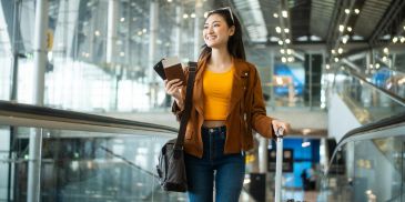 Young woman walking in an airport with luggage and passport.
